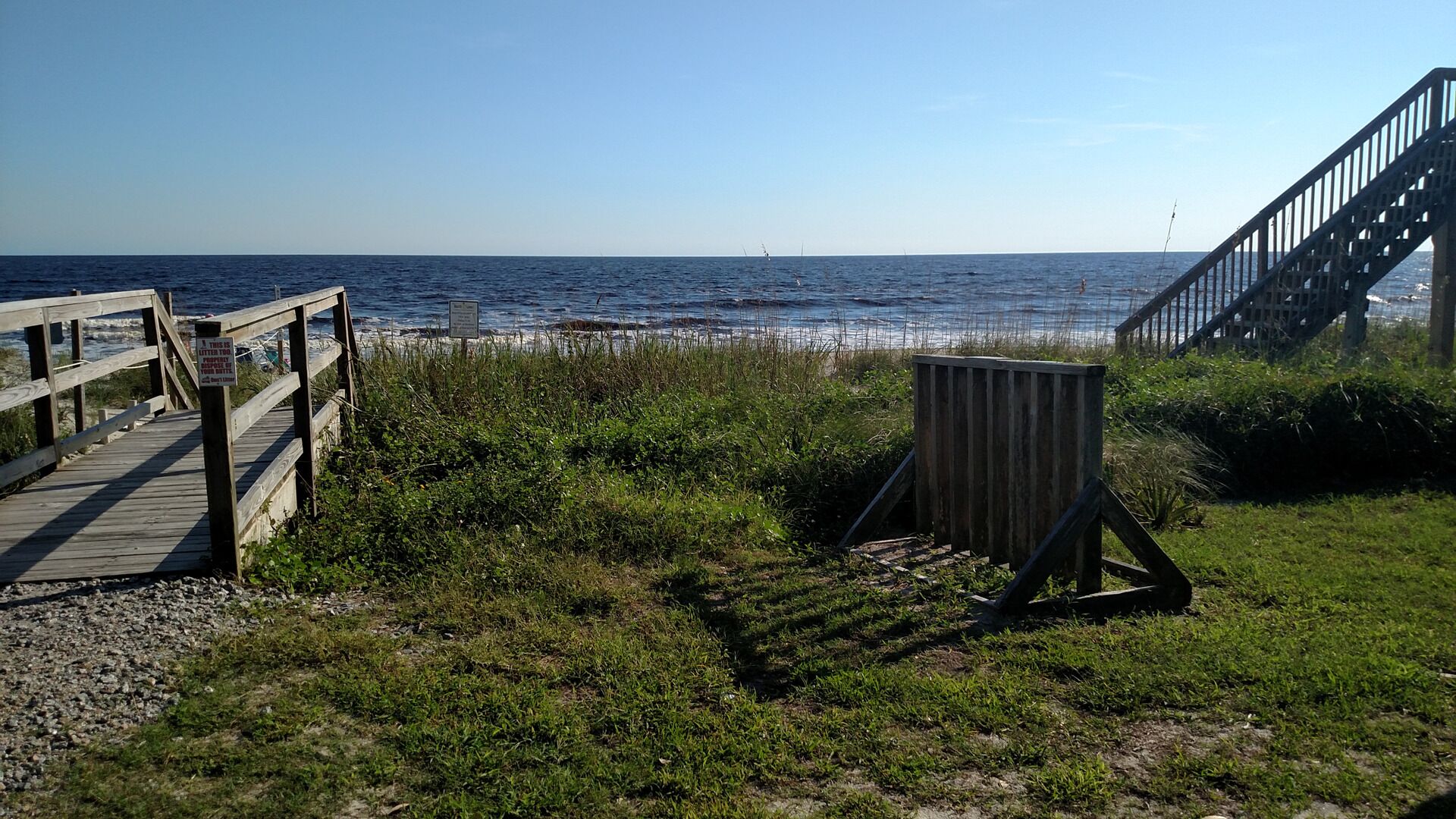 Une promenade en bois mène à une plage où se trouvent une structure en bois et un escalier.