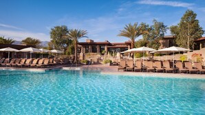 A pool area with lounge chairs and umbrellas, surrounded by palm trees and a building with a brick facade.