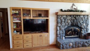 Una sala de estar con chimenea de piedra, mueble de entretenimiento de madera y televisor de pantalla plana.