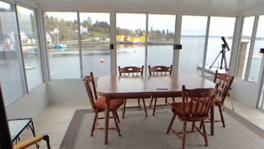 Una habitación con una mesa grande y sillas, ventanas amplias con vistas al agua y edificios, y un trípode en una esquina.