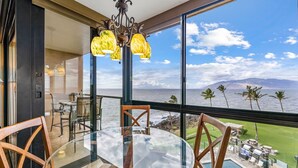 A glass table with chairs in a room with a view of the ocean and a pool area. - 505 – Lovely Oceanfront 1/1.5 unit – great ocean view with A/C! (Kihei)