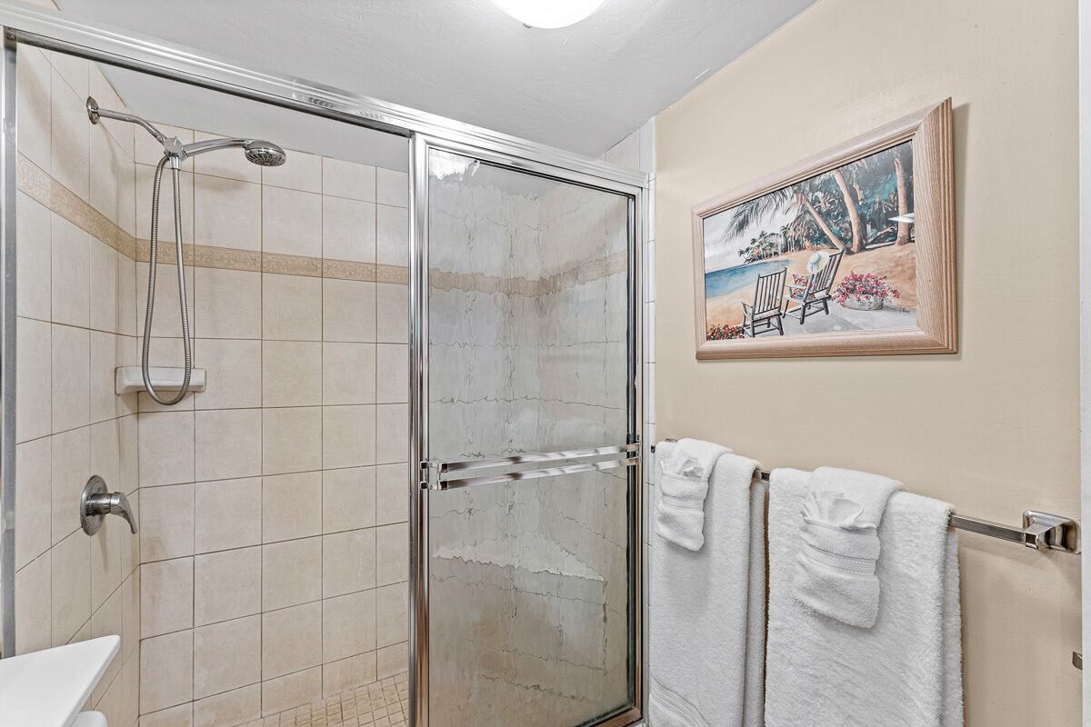 A bathroom with a glass-enclosed shower, a white sink, and a framed painting on the wall.