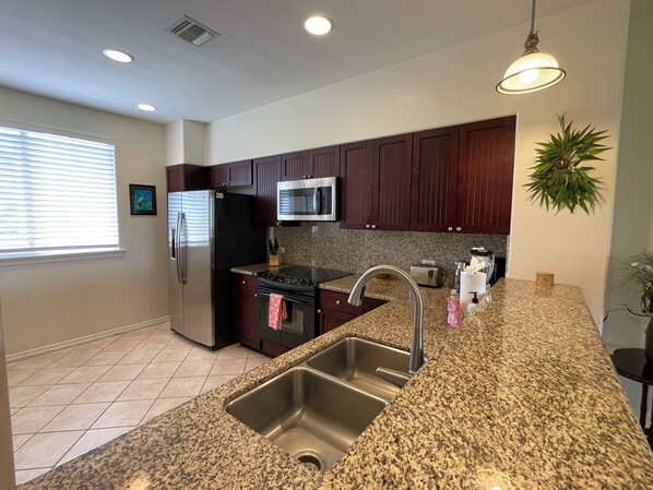 A modern kitchen with granite countertops, stainless steel appliances, and dark wooden cabinets. - Spacious and comfortable - Extended Stays Welcome (Waikoloa)