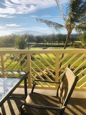 A patio with a table and chair, overlooking a golf course with palm trees and a clear sky. - Spacious and comfortable - Extended Stays Welcome (Waikoloa)
