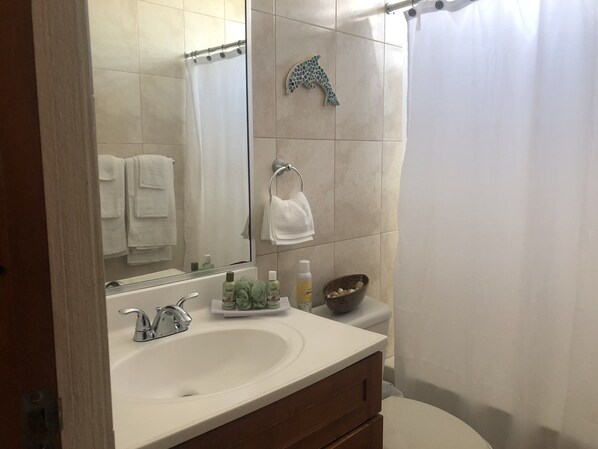 A bathroom with a white sink, a mirror, a shower curtain, and a tiled wall.