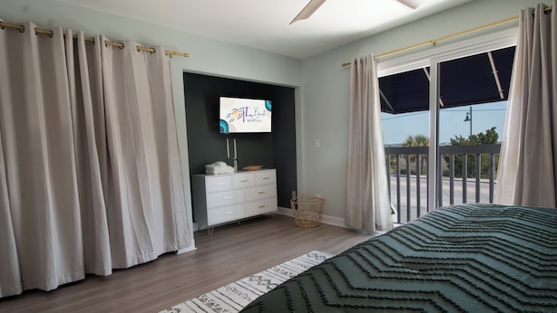 A bedroom with a bed, a TV, a dresser, and a balcony with curtains. - 1Br/1Ba Close to Beach & Shops- Heron's Nest (Folly Beach)