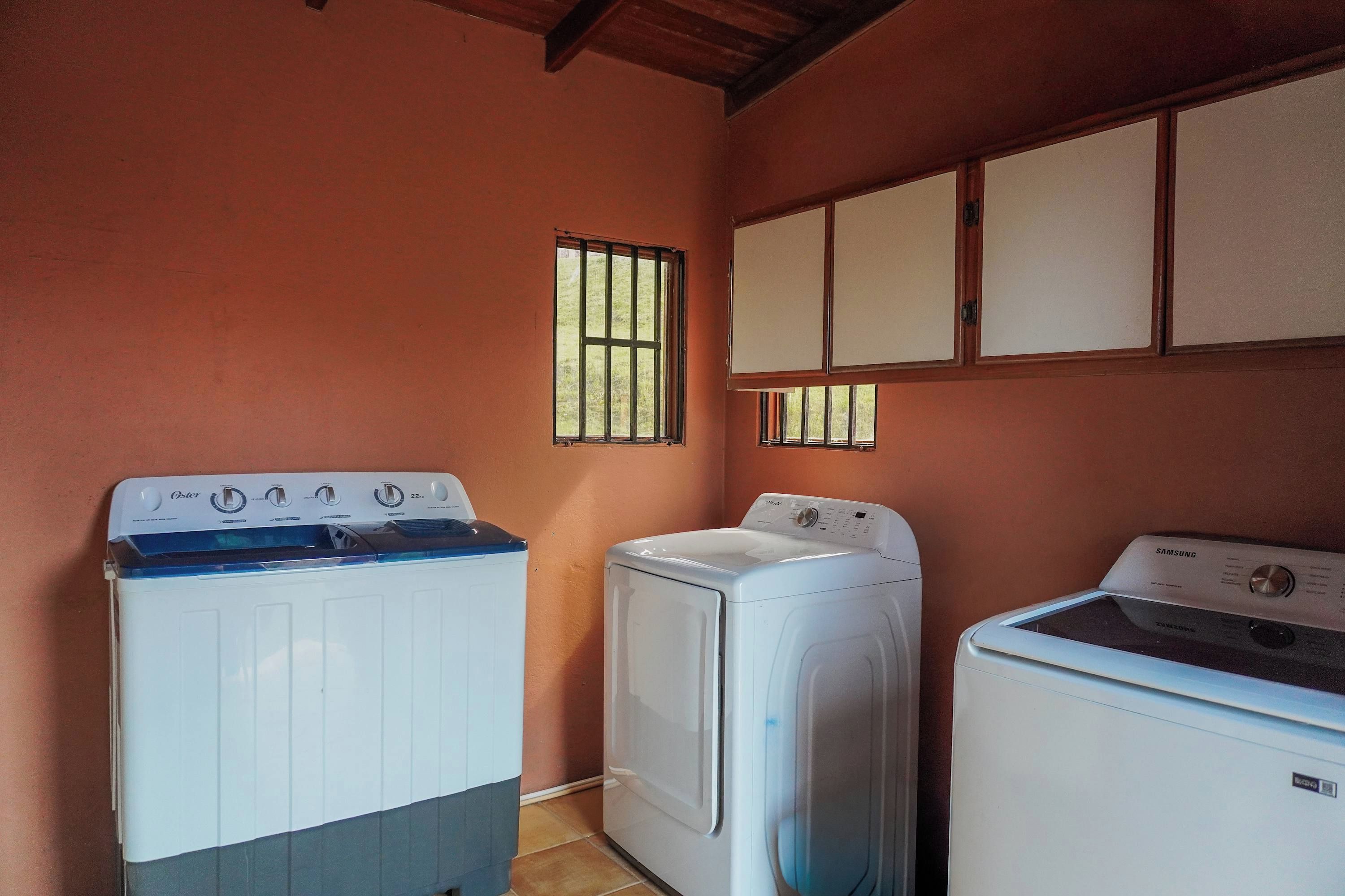 A laundry room with three washing machines, a window, and cabinets.