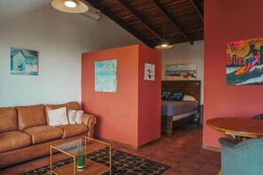 A living room with a brown sofa, a coffee table, and a small dining table. There are paintings on the walls and a bed in the background. - Heated Infinity Pool Villa, 6BR, 25Min SJO (Alajuela)