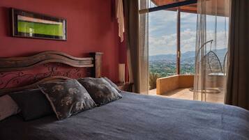 Un dormitorio con cama, almohadas, un cuadro enmarcado y un balcón con vistas.
