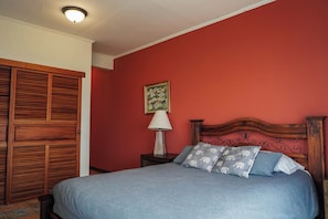 A bedroom with a bed, a nightstand, a lamp, a wooden headboard, and a red wall. - Heated Infinity Pool Villa, 6BR, 25Min SJO (Alajuela)