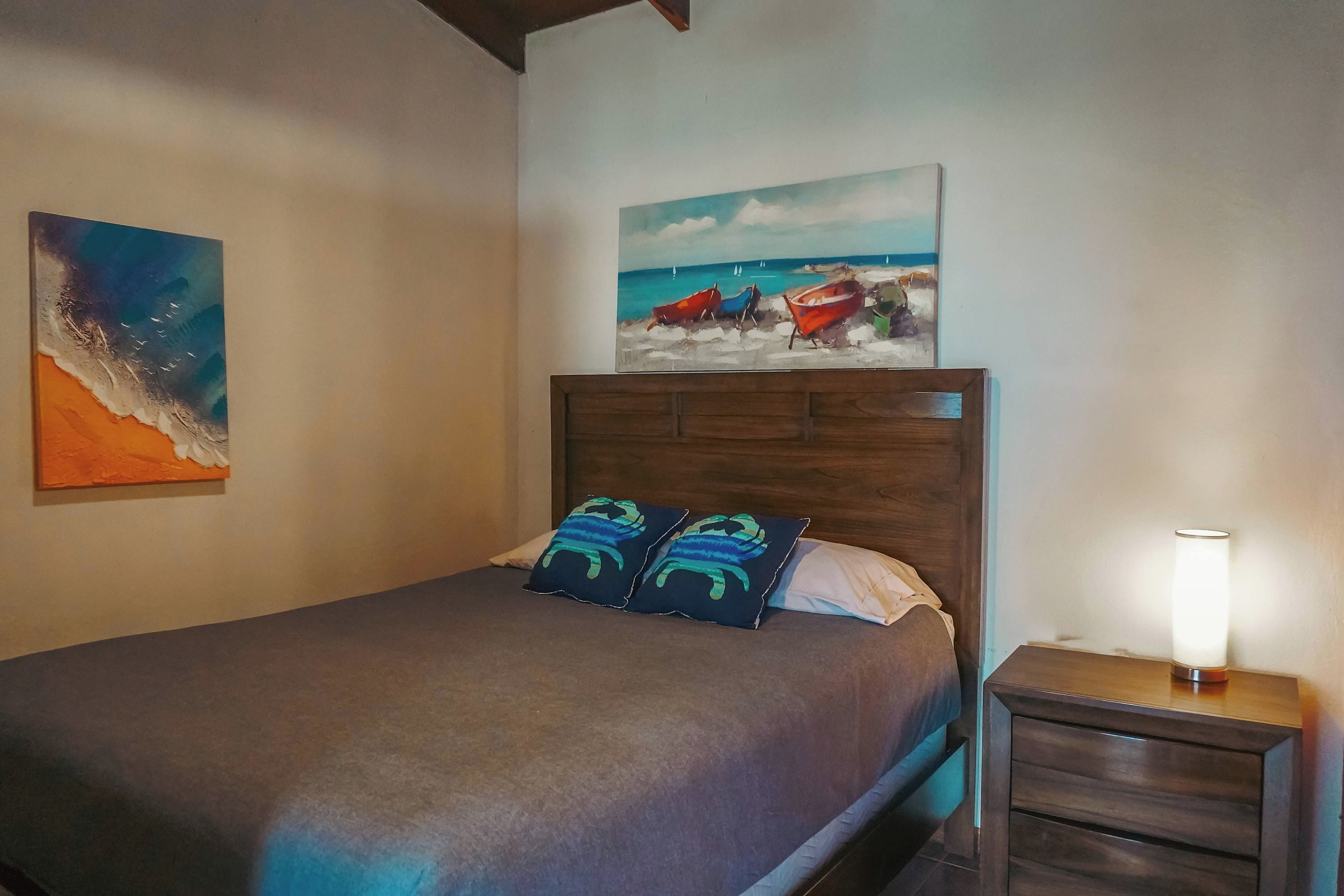 Ein Schlafzimmer mit einem Bett, zwei Kissen, einem Nachttisch, einer Lampe und zwei Bildern an der Wand.