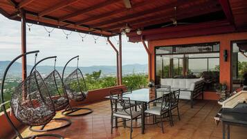 Une terrasse extérieure avec une table et des chaises, un fauteuil suspendu et une vue sur la ville et les montagnes.