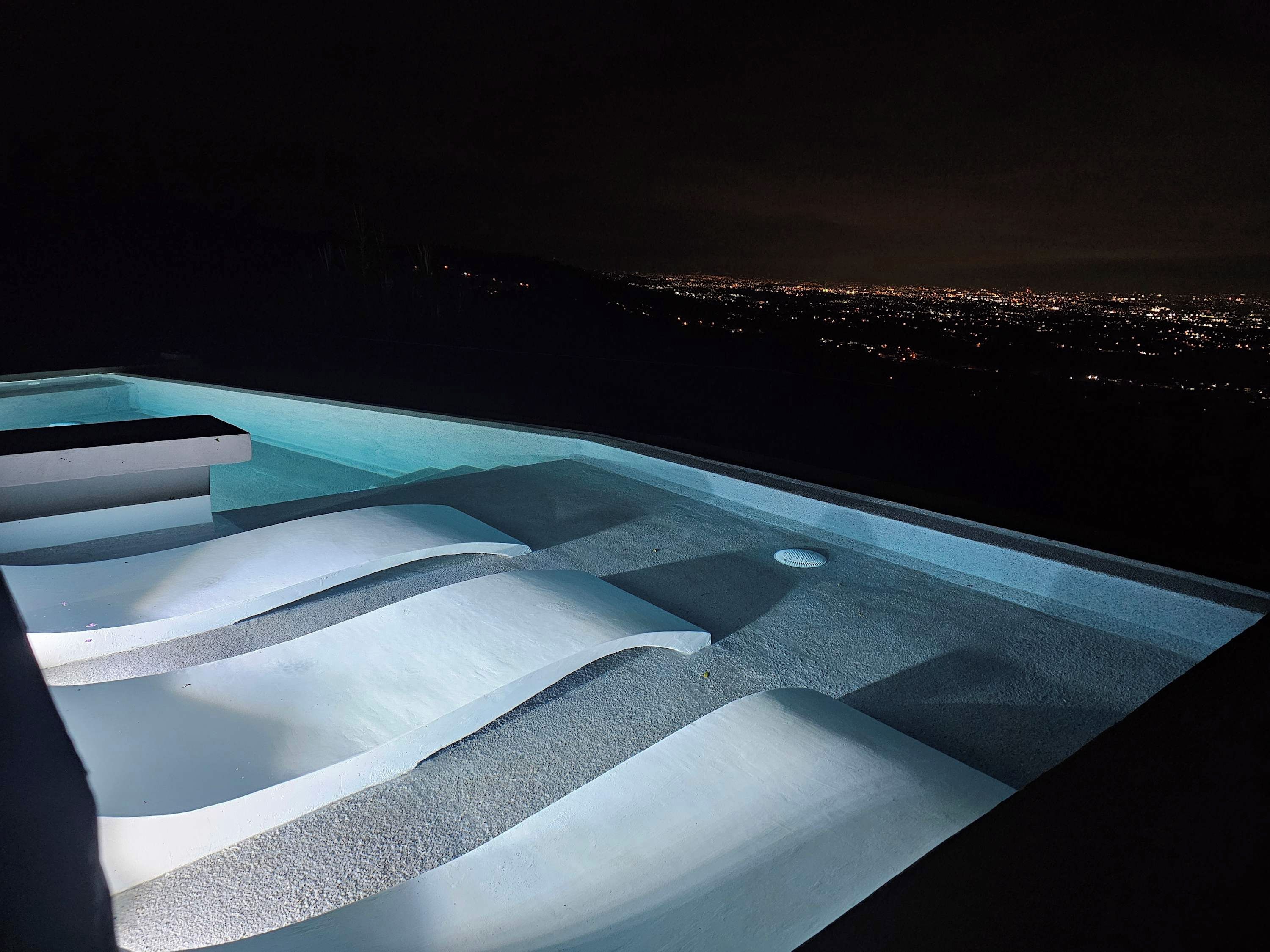 Una piscina infinita con niveles escalonados y vista a la ciudad de noche.