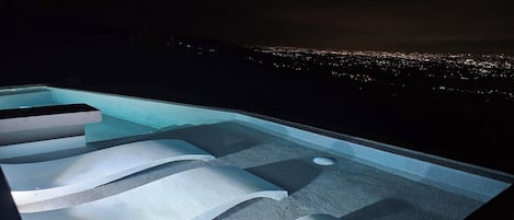 Una piscina infinita con niveles escalonados y vista a la ciudad de noche.