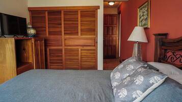 A bedroom with a bed, a wooden wardrobe, a television, and a lamp.