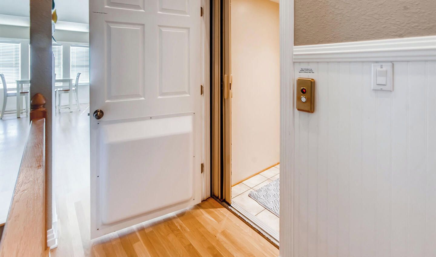 A hotel room entrance with a wooden floor, a white door, and a wall-mounted light switch.