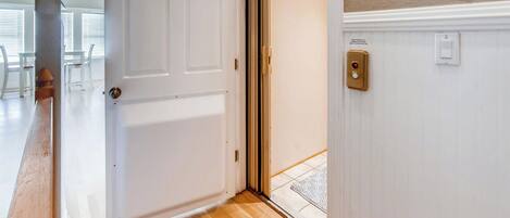 A hotel room entrance with a wooden floor, a white door, and a wall-mounted light switch.