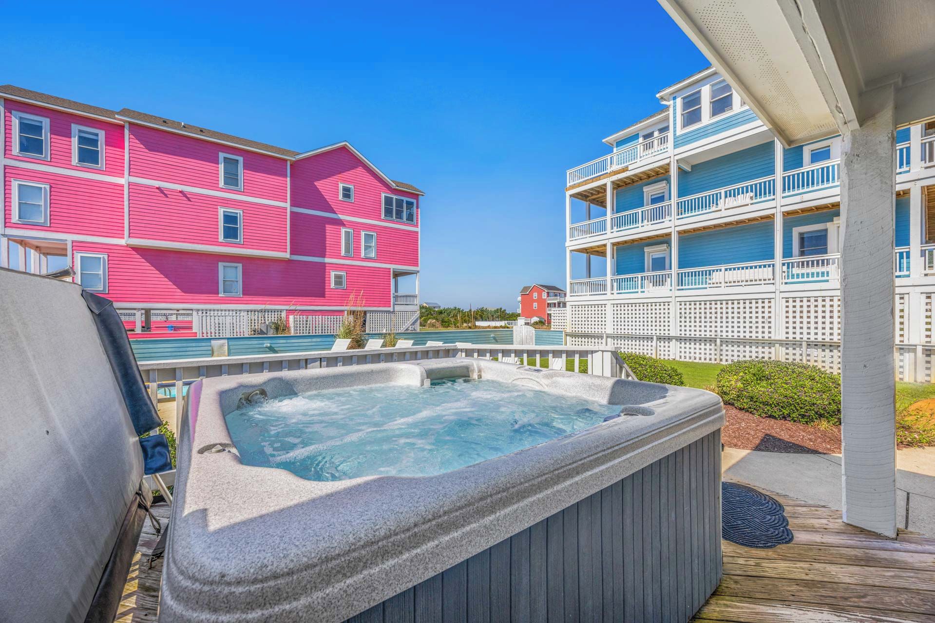Un jacuzzi en una terraza de madera con vistas a un edificio rosa y otro azul con balcones.