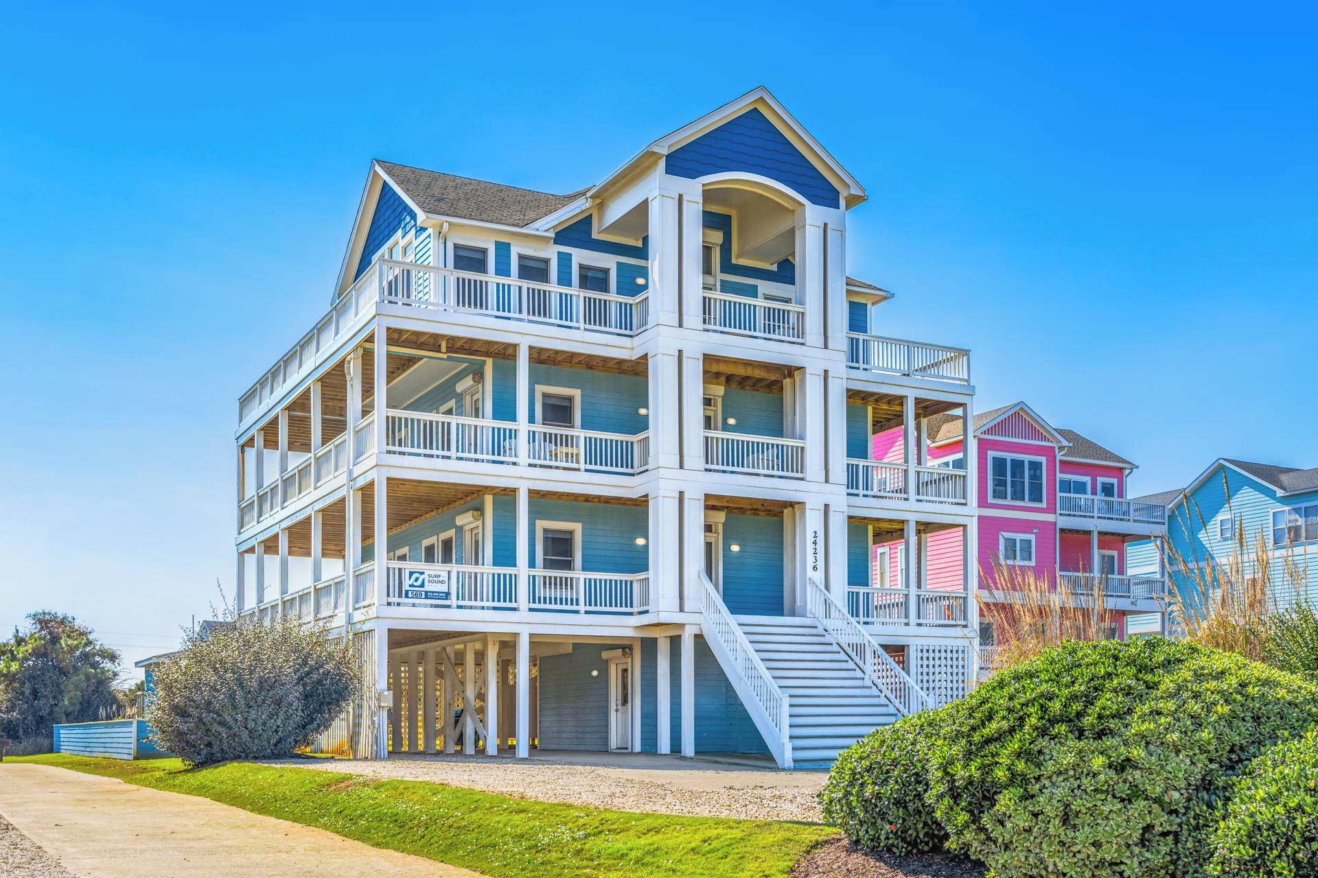 Une propriété en bord de mer, composée de plusieurs étages, dotée de balcons, d’un porche abrité et offrant une vue sur un ciel dégagé.