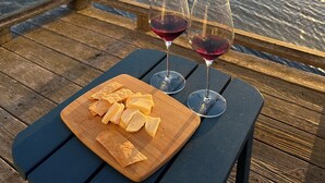 Een houten terras met een tafel waarop twee glazen rode wijn en een houten snijplank met plakjes kaas staan.