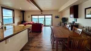 Een ruime keuken met een houten eettafel en stoelen, een rode bank en uitzicht op de zee door grote ramen.