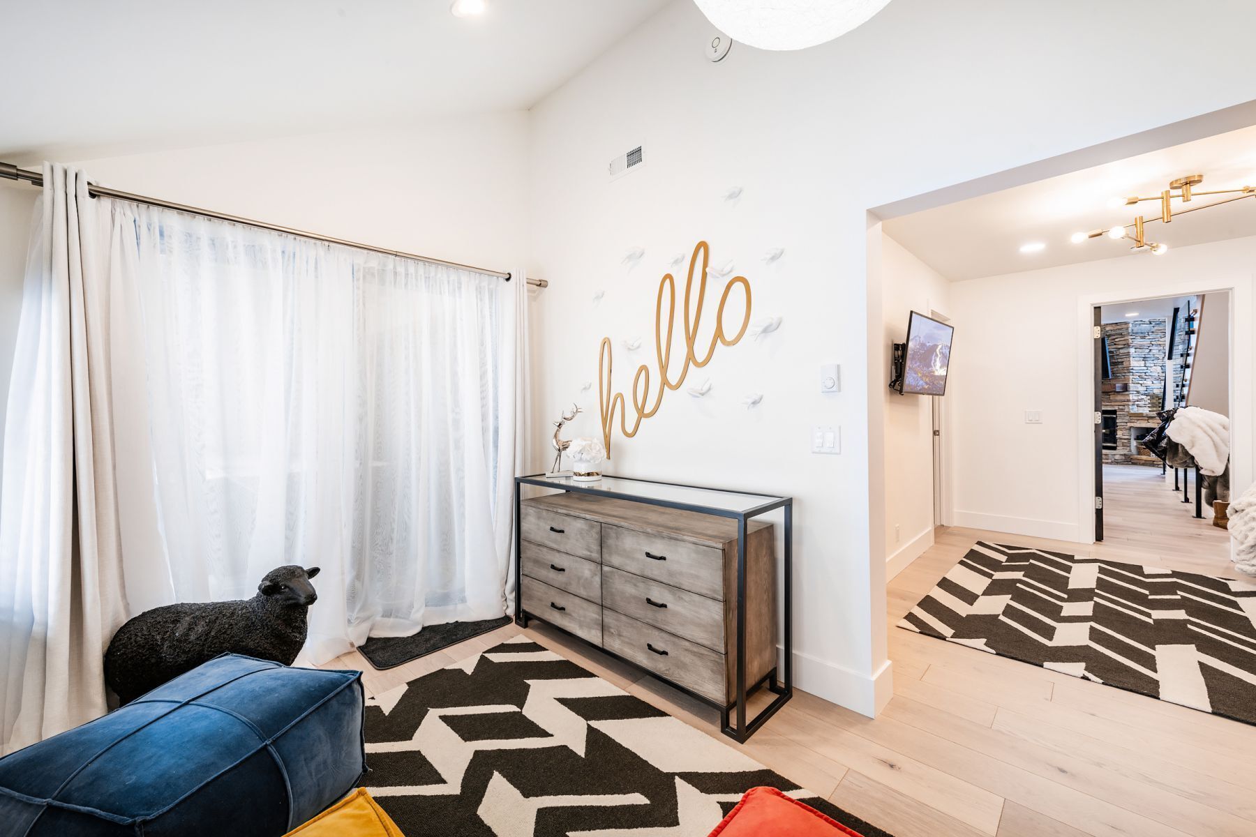 Ein modernes Wohnzimmer mit großer Wandkunst mit dem Schriftzug 'hello', einem Sofa, einem Couchtisch und einer dekorativen Schaf-Statue.