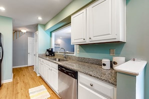 Kitchen features a dishwasher, sink, and coffee maker, with a window above the sink and a door to another room.