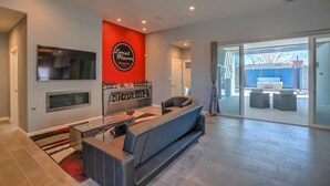 Un salon moderne avec un canapé gris, un mur d’accent rouge, un téléviseur fixé au mur et un meuble à vin.