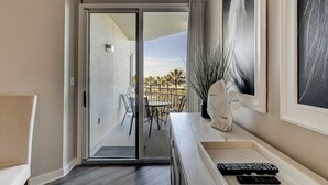 Ein Zimmer mit einer Schiebeglastür, die auf eine Außenpatio führt, einem weißen Konsolentisch mit einer Vase und Fernbedienungen sowie einem großen abstrakten Gemälde an der Wand.