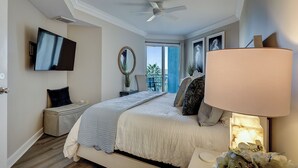 Ein Schlafzimmer mit einem Bett, einem Deckenventilator, einem Fernseher, einem Fenster mit Ausblick und einem Nachttisch mit Lampe.