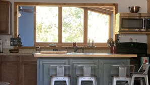 Une cuisine dotée d’un grand îlot central, de tabourets de bar, d’un four à micro-ondes et d’une fenêtre donnant sur la verdure.