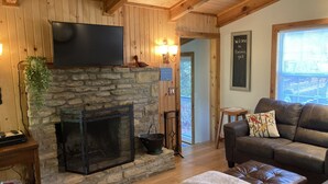 Un salon chaleureux avec une cheminée en pierre, un canapé en cuir et un téléviseur à écran plat fixé au-dessus de la cheminée.