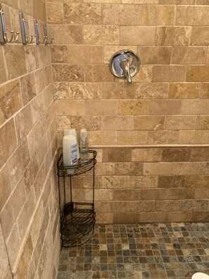 A bathroom with a tiled floor, a shower with a chrome faucet, and a small shelf with toiletries.