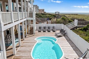 Une piscine sur le toit, avec une terrasse en bois, des chaises longues et une vue sur l’océan.