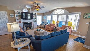 A spacious living room with a fireplace, blue sofas, and a television. - Luxury Oceanfront Retreat: Concierge Beach Tent Service, Private Pool & Elevator (Holden Beach)