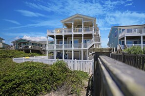 A multi-story beachfront property with balconies, a wooden deck, and a view of the ocean. - Luxury Oceanfront Retreat: Concierge Beach Tent Service, Private Pool & Elevator (Holden Beach)