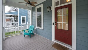 En veranda med en rød dør, en loftsvifte og en teal Adirondack-stol.