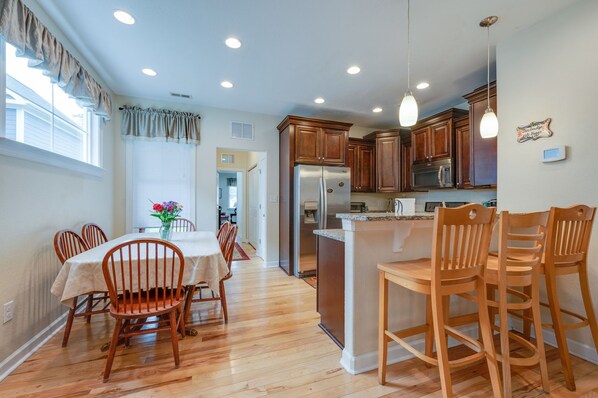 A modern kitchen with wooden cabinets, a stainless steel refrigerator, and a dining area with wooden chairs and a table.