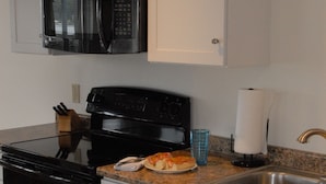 A kitchen with white cabinets, a black microwave, a stove, and a sink. -  Unique Marina Side Condo With Great Views And Fun Atmosphere! (Southwest Harbor)