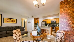 A living room with a sofa, patterned armchairs, a coffee table, and a decorative sculpture. A kitchen with wooden cabinets and modern appliances is visible in the background. - SLEEPS 6 Beautiful, Fully Furnished Condo - Great Price, Perfect Location! (Tempe)
