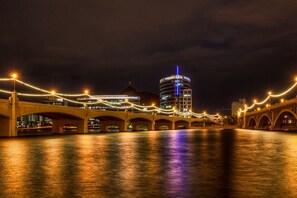 Vista nocturna de un puente con luces iluminadas y un edificio moderno al fondo.