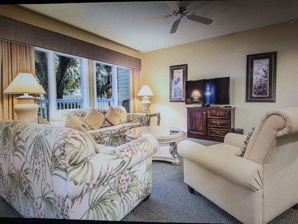 A living room with a sofa, armchairs, a coffee table, a TV, and a ceiling fan.
