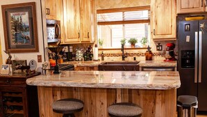 Una cocina con armarios de madera, encimera de granito, un lavamanos, un refrigerador y dos taburetes.