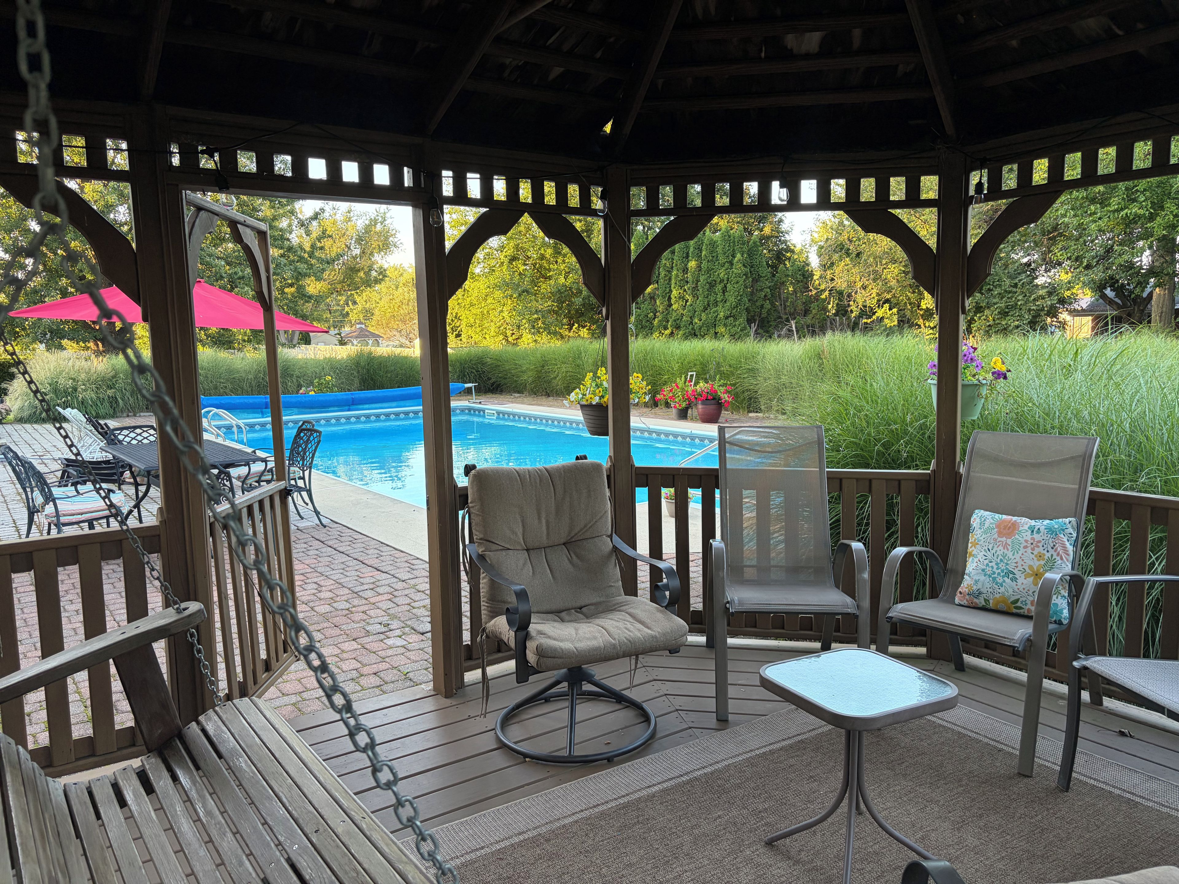 A covered outdoor area with a pool, seating, and a view of the surrounding greenery.