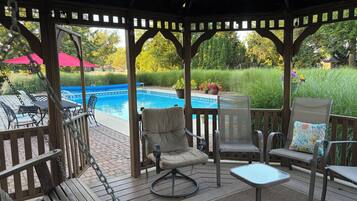 A covered outdoor area with a pool, seating, and a view of the surrounding greenery.