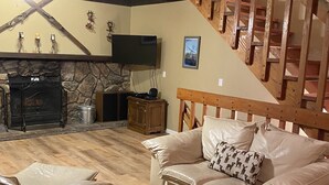 A cozy living room with a stone fireplace, a wooden staircase, and a beige sofa with patterned cushions. - Perfect Family Getaway,  One Light to Snow Summit, Bear Mountain and Shopping (Big Bear Lake)