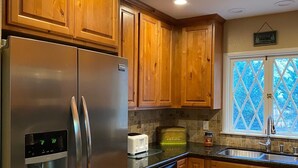 A kitchen with wooden cabinets, a stainless steel refrigerator, a toaster, and a window with a view of trees. - Perfect Family Getaway,  One Light to Snow Summit, Bear Mountain and Shopping (Big Bear Lake)