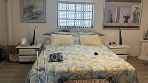 A bedroom with a bed, bedside tables, a window with blinds, and artwork on the walls.