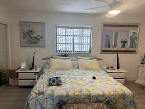 A bedroom with a bed, bedside tables, a window with blinds, and artwork on the walls. - Oceanfront Sandy Beach Vacation Rental Unit 1 (Marathon)