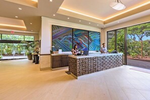 A reception area with a modern design, featuring a reception desk, a large abstract painting, and large windows with a view of greenery.